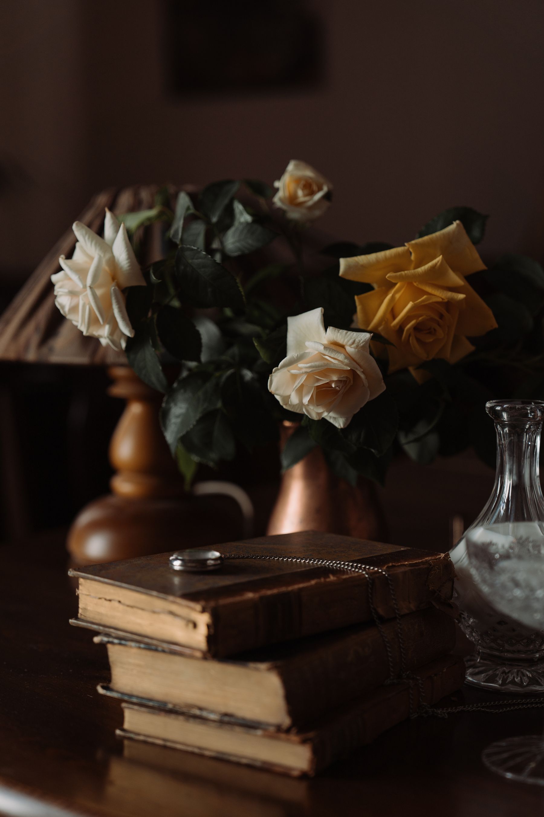 Cream roses in a brass pitcher beside a stack of books
